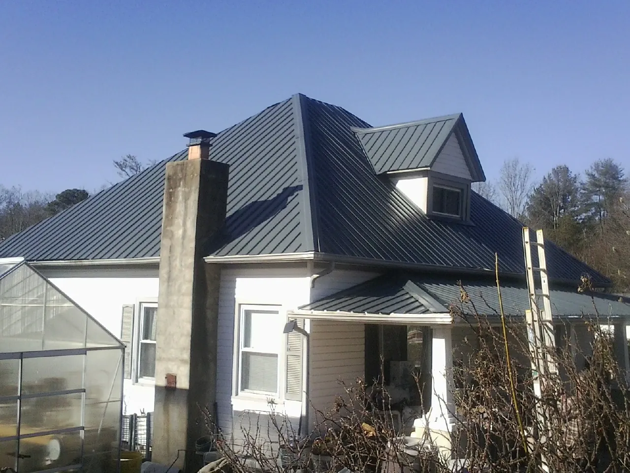 Dark blue standing seam metal roof on a white farmhouse with dormer — Slate & Tile Roof Repair by Roofing Brothers in Pierz