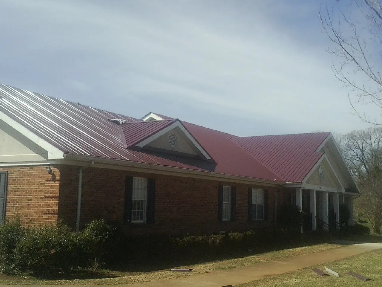 Red metal roof with gabled entries on a long brick building, from a Hail Damage Roof Repair job in Pierz