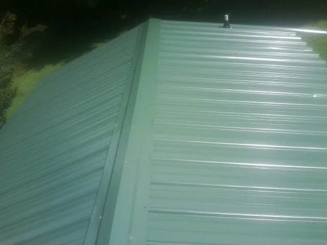 New green metal panels meeting at the ridge of a roof — Flat Roof Repair work by our crew in Pierz
