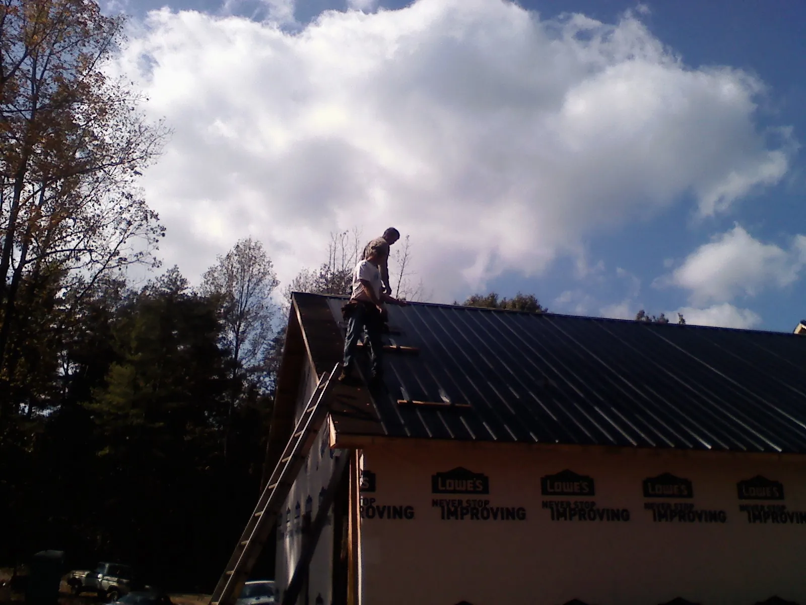 Roofer fastening dark metal panels high against a cloudy sky, from a Roof Inspection job in Pierz