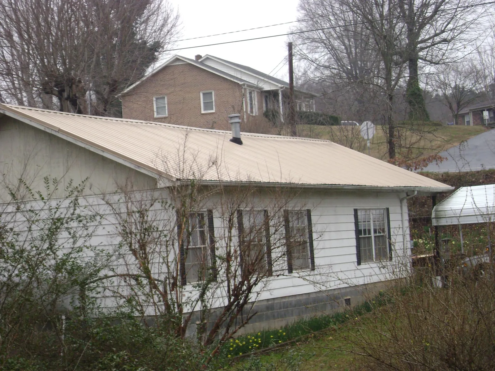 Tan metal roof on a white sided house set into a hillside — Commercial Roofing by Roofing Brothers in Pierz