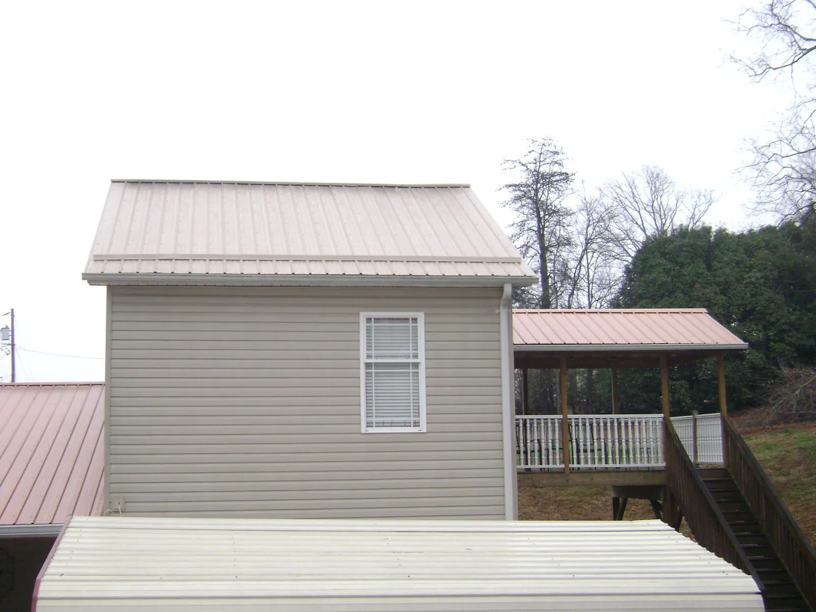 Tan metal roofs on a two story addition and attached porch, from a Roof Replacement job in Pierz